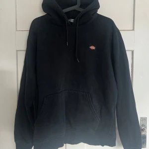 Svart hoodie från Dickies - Säljer en klassisk svart hoodie från Dickies med en liten logga på bröstet. Den har en stor ficka framtill och justerbar huva med dragsko. Perfekt för en avslappnad stil.