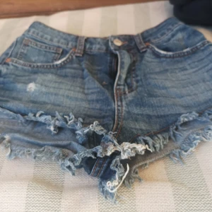 Jeansshorts med fransar från Lindex - Snygga jeansshorts från Lindex med fransiga kanter och klassisk femficksdesign. Perfekta för sommardagar och festivaler. De har en knapp och dragkedja framtill för enkel stängning.