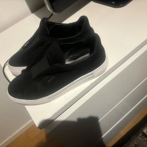Svarta sneakers från Axel Arigato laceless  - Snygga svarta sneakers från Axel Arigato. Skorna har en stilren design med vit sula. Fick dessa i födelsedagspresent men det var en storlek för liten. Ny pris går för 2600