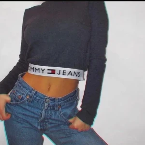 Mörkblå croppad tröja från Tommy Jeans - Säljer en mörkblå croppad tröja från Tommy Jeans med en elastisk kant med logotypen i midjan. Tröjan har långa ärmar och en stilren design. Perfekt för en avslappnad look.