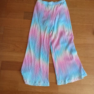Färgglada plisserade byxor - Säljer ett par färgglada plisserade byxor i regnbågens färger. Byxorna har en loose passform och är perfekta för en somrig look. De är elastiska i midjan för extra komfort. Har aldrig använts, prislappen är fortfarande på. 