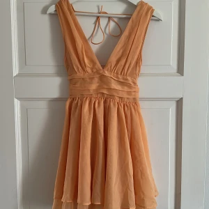Aprikos klänning från Abercrombie & Fitch - Så vacker aprikos klänning från Abercrombie & Fitch. Klänningen har en v-ringad design med knytband i ryggen och en luftig kjol. Perfekt för varma dagar eller speciella tillfällen.
