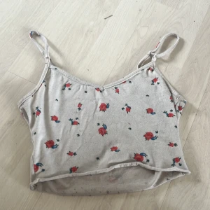 Beige blommig linnetopp - Söt beige linnetopp med röda blommor och smala axelband. Perfekt för varma sommardagar. Toppen har en avslappnad passform och är lätt att matcha med jeans eller shorts.