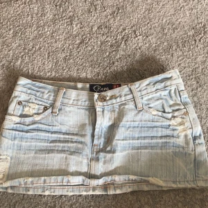 Ljusblå jeanskjol från Ben - Trendig ljusblå jeanskjol från Ben med slitna detaljer och broderade fickor. Perfekt för en avslappnad stil. Kjolen har en klassisk femficksdesign och knappstängning fram.