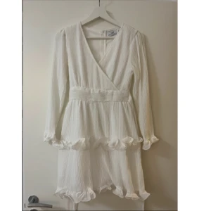 Vit omlottklänning med volangdetaljer - Säljer en vit klänning från Dressy med v-ringning och volangdetaljer vid ärmslut och nederkant. Perfekt för studenten!🤍