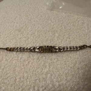 Armband från Dior med kristallblad - Elegant armband från Dior med gnistrande kristallblad och bokstäverna DIOR i mitten. Perfekt för att ge en lyxig touch till din stil.