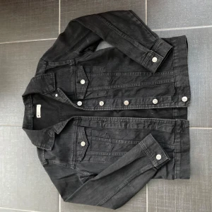 Svart jeansjacka med knappar - Snygg svart jeansjacka med knappar framtill och två bröstfickor. Jackan har en klassisk krage och långa ärmar. Perfekt för en cool och avslappnad stil. Aldrig annvänd och i storlek S, säljer pga av att den är för liten 💗