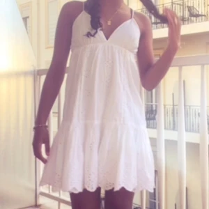 Vit ärmlös klänning - Söt vit klänning med broderade detaljer och v-ringad hals. Den är ärmlös och har en luftig passform, perfekt för varma sommardagar. Klänningen har en lätt volang nedtill som ger en romantisk känsla.