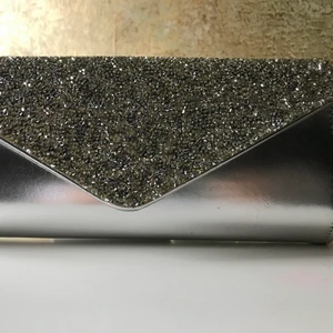 Glittrig kuvertväska - Väskan öppnas med magnetlås, har en mindre ficka på insidan och kan även bäras över axeln med en silverkedja. Passar bra till en festkväll.