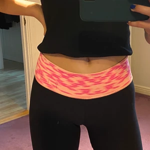 Träningstights PINK (victoria’s secret) - Svarta träningstights ifrån PINK. Går att ha tightsen både ut och in. Midjebandet ena hållet är ljus orange och rosa färgat. Andra hållet är endast ljus orange med PINK text bak.  Nypris: 60$. Fraktavgiften står köparen för!💫