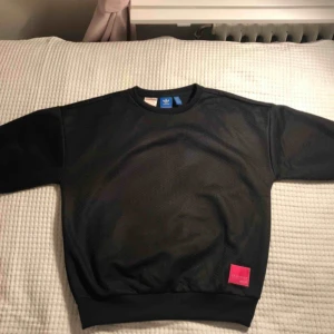  -  Svart Adidas collegetröja med  mönster, det syns inte tydligt vid första anblick utan syns mest på nära håll men ger ändå en cool effekt. 3/4 ärm. Liten rosa detalj längst ner till vänster. Storlek 12-13y i barnmodell men passar en S eller M.