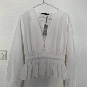 Vit skjortaktig topp - Säljer denna vita skjortaktiga topp. Köpt på Bik Bok och är aldrig använd. Prislappen sitter kvar. Kan antingen mötas upp eller så står köparen för frakten!