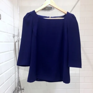  - Djupblå blus med vida 3/4 ärmar och dragkedja på ryggen. 
