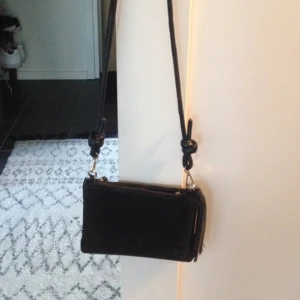  - Crossbody väska i svart med gulddetaljer från Day Birger det Mikkelsen, köpt för 1099:- 2015. Skinn och mocka med tofs som är avtagbar. Består av ett rundat långt axelband samt två clutchdelar, En i svart mocka och en i svart krockoskinn som också går att knäppa loss och använda separat. Mycket fint skick! 