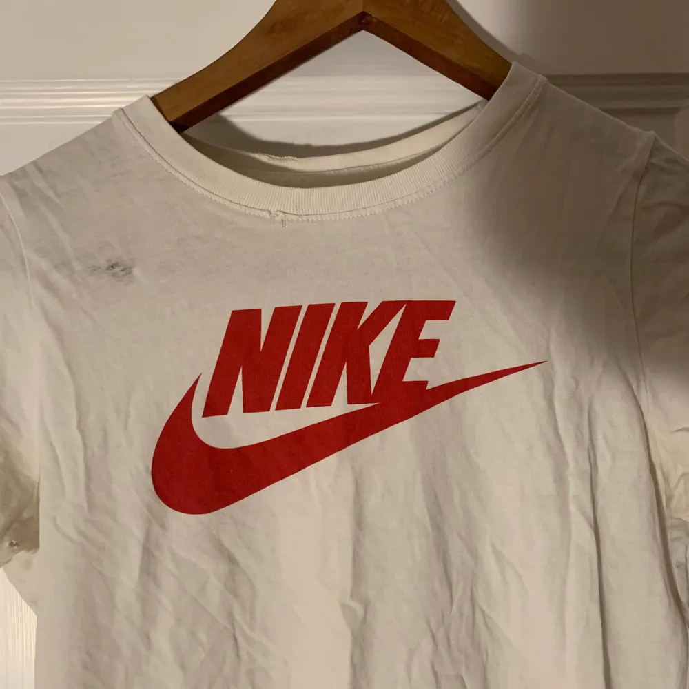 Vit Nike T-shirt med röd logga/swoosh i jätteskönt material. Strl XS. (Obs! Ser ur som en fläck vid bröstet på bilden men är som ett litet hål/tyget har blivit slitet där men syns ej när man har den på sig) . T-shirts.