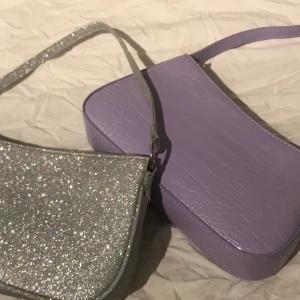 Axelväska - Två stycken trendiga axelväskor som inte kommer till användning. Båda är knappt använda och i nyskick. Rymliga båda två. 100+frakt för den lila. Glittrig såld