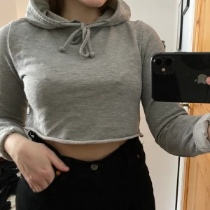 Grå croppad hoodie - Fin grå ganska kort croppad hoodie med ”rivmärken” på axlarna. Väldigt skönt material. Är köpt utomlands och kommer ej ihåg vad butiken hette. Använd men i fint skick. 