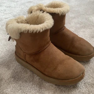 Äkta Uggs med rosett - Fina äkta uggs, men rosett där bak⚡️flitigt använda som ni kan se på bild tre. Passformen är fortfarande väldigt bra! Otroligt sköna och man fryser aldrig i dom!💕storlek 36. Nypris: runt 2000kr, mitt pris: 100kr+frakt. Sjukt bra pris!🤩