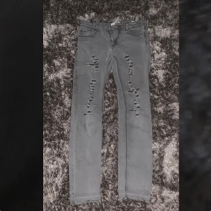 Jeans med hål/slitningar  - Säljer ett par gråa jeans i storlek 34 (164 cm) som har hål/slitningar. Sparsamt använda. Kan skickas, men då står köparen för frakt för ca 30/40kr.