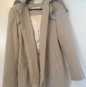 ”Damjacka Calvin Klein” - Damjacka Calvin Klein. Kall beige färg. Storlek 34-36. Fint skick bortsett från fläcken (se bild). Med extra omtanke kan fläcken gå bort. Jackan är välsydd, har avtagbar luva, snyggt skärp med smart och smidigt knäppe. Dragsko på insidan av jackan. Den finns i Jönköping annars kan jag skicka den och då står du för frakten. Vill du köpa den så hör av dig! 🙂 