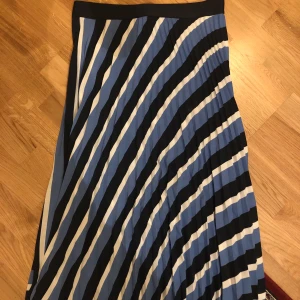 Plisserad kjol strl M - Plisserad, vadlång kjol med vita, blåa och svarta ränder. 