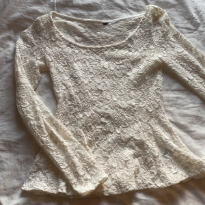 Vit spets tröja - Tröjan är kroppssydd med utsvängd volang längst ned, långa ärmar och bred urringning. Bra skick och använd endast ett fåtal gånger. Lappen om strlk är bortklippt men passar som 152/164