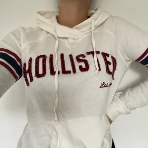 Hollister hoodie  - En mysig vit hoodie från Hollister med röda och blåa detaljer. Storlek XS. Fin passform!