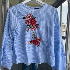 Blus Bik Bok - Blåvit randig blus från Bik Bok med blomdetaljer och vida flairarmar. Super fint skick och köparen betalar frakten🌸