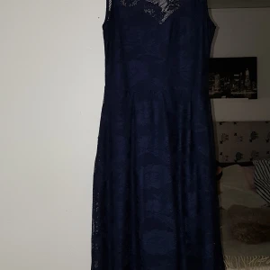 Mörkblå klänning i spets  - Mörkblå medellång klänning i blommigt spetstyg. Klänningen är i storlek 40 och är bra i storleken, inte för stor för att vara en 40. Jag har själv köpt den begagnad men den är i ett fint skick.