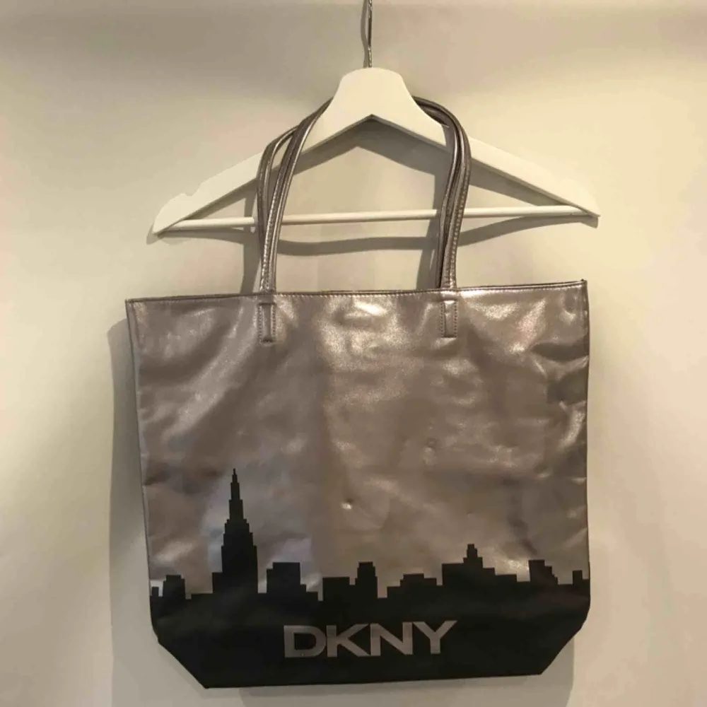 Supersnygg silvrig väska med svart stadssilhuett på från DKNY! Säljer eftersom den får alldeles för lite uppmärksamhet i min garderob.. Väskor.