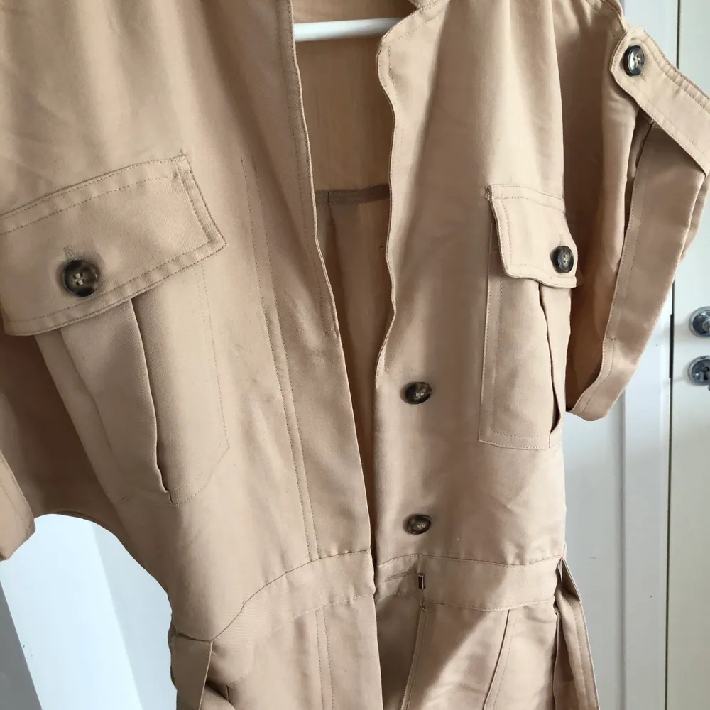 Beige jumpsuit från HM i storlek 36! Använd fåtal gånger. Har ett bälte i midjan och knappar samt blixtlås framtill 😍 100kr . Klänningar.