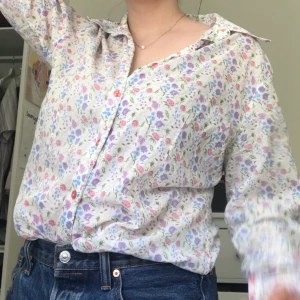 blommig blus - jättesöt vit blus med små blommor på och rosa knappar. skulle säga att den har lite 70tals vibe för kragen är lite "längre" och spetsig typ. inte så extremt alls dock. perfekt skick förutom att en knapp saknas på ena ärmen. den är tunn men inte så genomsk