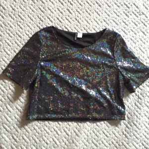  - Crop top med paljetter! Kortärmad t-shirt med silvriga paljetter som skiftar i rengbågsfärger. Tröjan är svart i grunden och har en undertröja. Slutar ovanför naveln. 

Köparen betalar frakt, kan annars hämtas i Göteborg. 