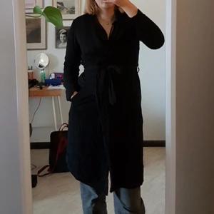 Kappa / Trenchcoat  - Tunnare svart kappa med knytning. Perfekt till hösten och våren! Jag är 176 cm lång och brukar ha S/M. Nyskick förutom en sömn som har gått upp i ena mudden, lätt att fixa. Frakt tillkommer.