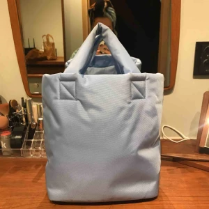 Blå puffig väska från Weekday - Blå puffig väska från Weekday. Endast använd ett fåtal gånger så är i gott skick. Den kommer även med en axelbandsrem.