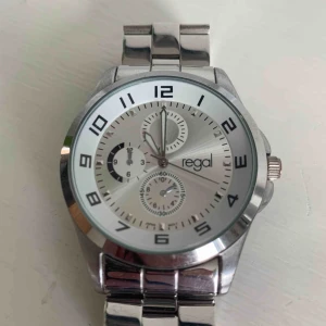  - Silverfärgad klocka från regal, finns lösa länkar att förlänga band med  Behöver nytt batteri Skickas mot fraktkostnad