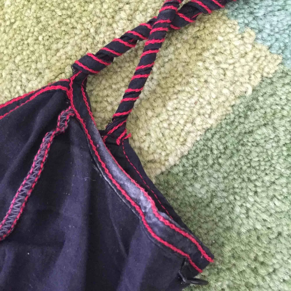 Desigual fin klänning i svart med brodyr i rött, rosa, grått och vitt. Snurrat band runt ena axelbandet behöver fästas och deofläckar behöver tas bort (bild 2). Även skada i tyget i nedre delen av dragkedjan (bild 3).. Klänningar.