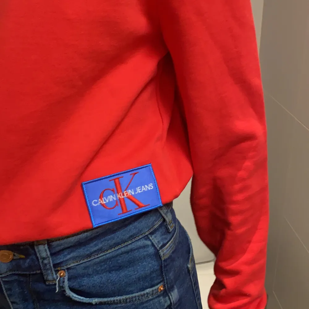 Röd Calvin Klein tröja med blått märke på sidan i strl Xs, aldrig använd förutom när vi skulle ta bilden✨. Tröjor & Koftor.