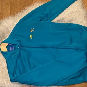 Adidas kofta i storlek xxs  - Fin blå adidas kofta i olika regnbågsfärger på bakdelen av ryggen. Passar även som storlek S och är i bra skick. Använt en gång. (Äkta).