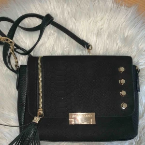  - Svart ”ormskinns” liknande handväska ifrån riverisland. Guldiga detaljer och axel rem Nypris 499