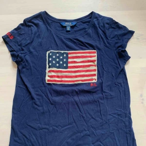  - Mörkblå t-shirt med amerikanska flaggan på från Polo (Ralph Lauren) i fint skick!