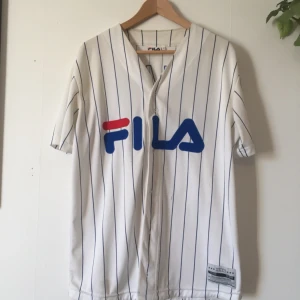  - Baseball tröja från FILA i samarbete med Junkyard. Storlek M. Använd men fortfarande i snyggt skick. Två tråddragningar, dock inget man lägger märke till direkt.  