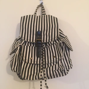  - Svart/Vit Randig Ryggsäck. Använd väl men fortfarande i bra skick. Dock har magneten åkt av (foto 3) så det går inte att stänga en av fickorna helt. Den mycket med utrymme och är väldigt enkel att bära med sig.