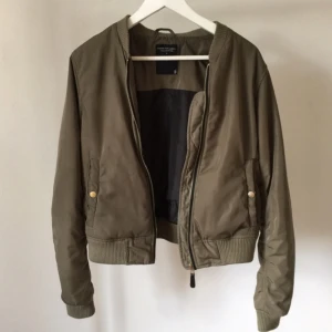  - En bomberjacka från Lager 157 i en militärgrön färg som passar bra till hösten! Sömmarna börjar bli slita och jag har sytt igen där det hade gått sönder vid fickorna (se bild 3). Även en söm på insidan av jackan är sydd. Annars är det en väldigt fin jacka och hoppas du vill ta över denna! 