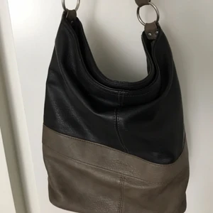 Ceannis axelremsväska - Väska från Ceannis, inte äkta läder. Mullvadsgrå/brun och mörkbrun. Skön form, flera innerfickor för småprylar. Inre dragkedja är sönder, även ena karbinhaken för axelremmen som medföljer.  Bredd: 34 cm Höjd: 11 cm Djup: 35 cm