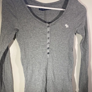 Grå aberceombie tröja - Tajt ribbad aberceombie tröja. Sitter väldigt fint och har knappar där fram. Perfekt att ha under T-shirtar!