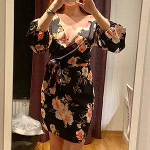 Blommig klänning - Långärmad blommig klänning från Nelly som tyvärr är lite för stor för mig. Dragkedja baktill. Svart med rosa blommor. Tunn och bekväm. Aldrig använd pga fel val av storlek. Köparen står för eventuell frakt