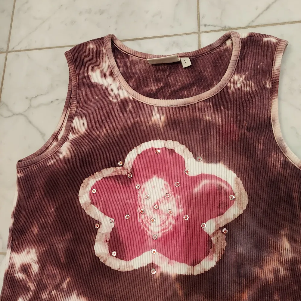 Ett batikfärgat linne med en rosa blomma🌸🌸 blomman har även små paljetter på sig vilket är fint och den passar verkligen in i early 2000's viben! Står L men passar definitivt mindre också (jag är S). Toppar.