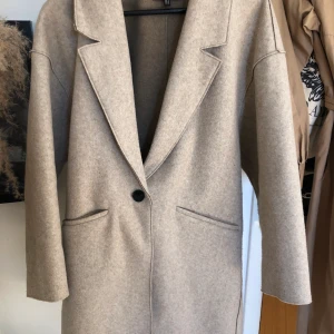 Zara kappa beige - En lite tunnare kappa i grå/beige färg från Zara, väldigt klassisk och snygg. Sparsamt använd och i gott skick! Den går ner till knäna ungefär på mig som är 170 cm lång.