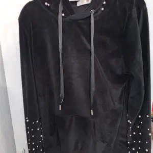 En svart hoodie från Madlady med vita pärlor på ärmarna och luvan. Hoodien är i satin material. 